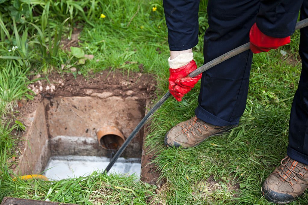 Drain being cleared by worker in navy overalls.